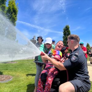 A fireman and a person in a wheelchair using a firehose.